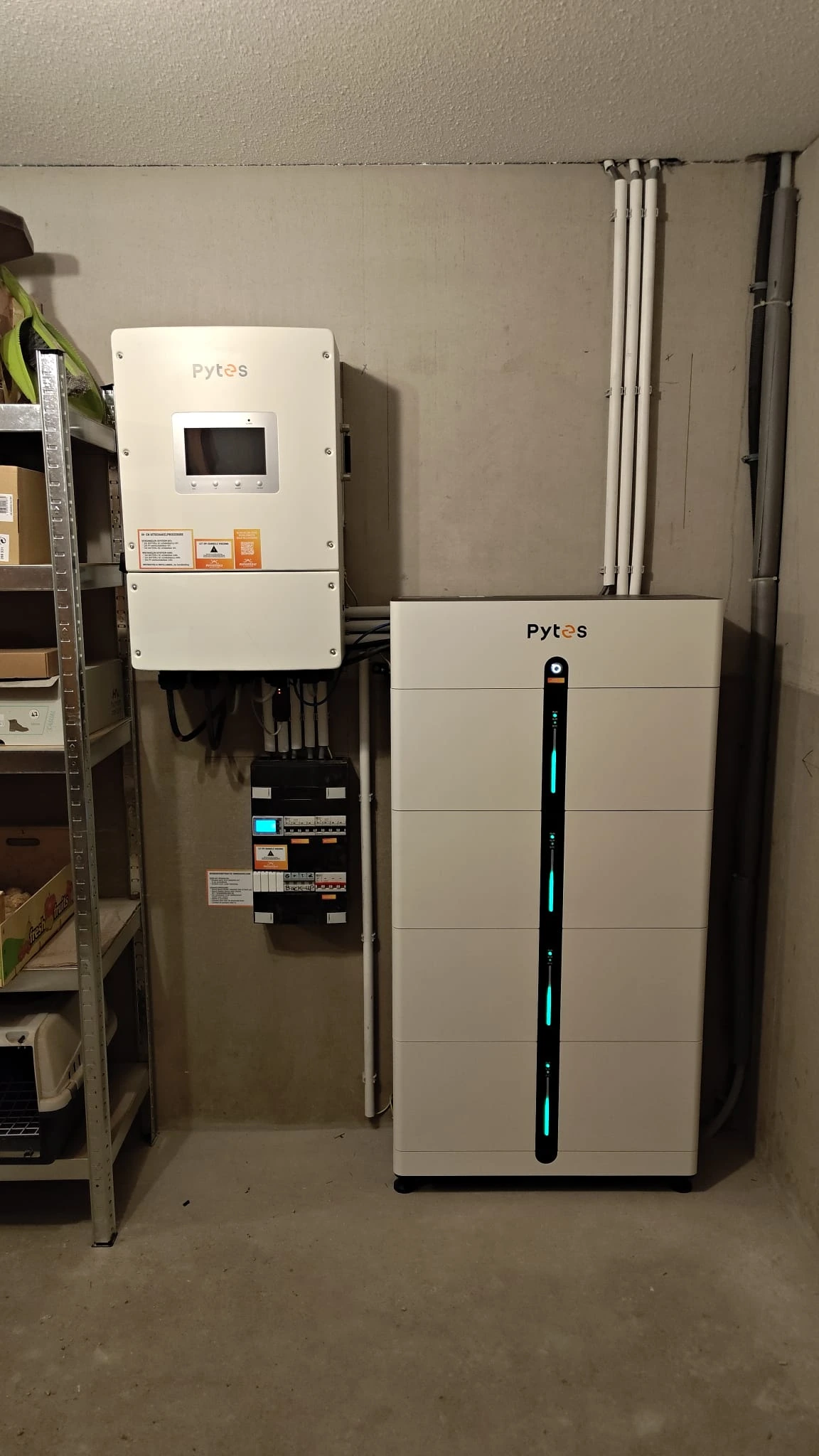 Echte Pytes thuisbatterij met verlichte statusbalk naast de omvormer in een kelderberging