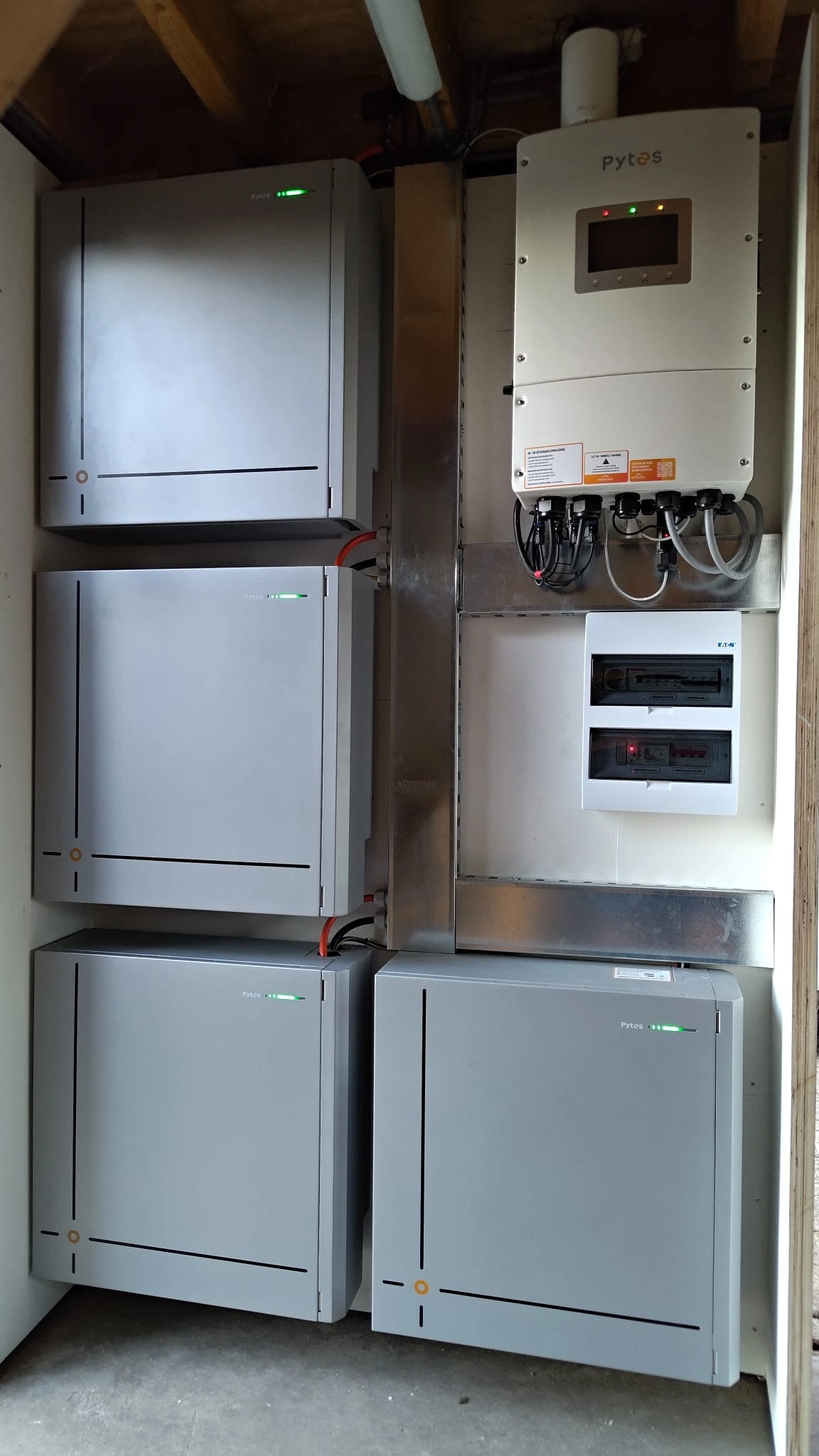 Echte opstelling van vier Pytes batterijmodules met omvormer in een houten bijgebouw